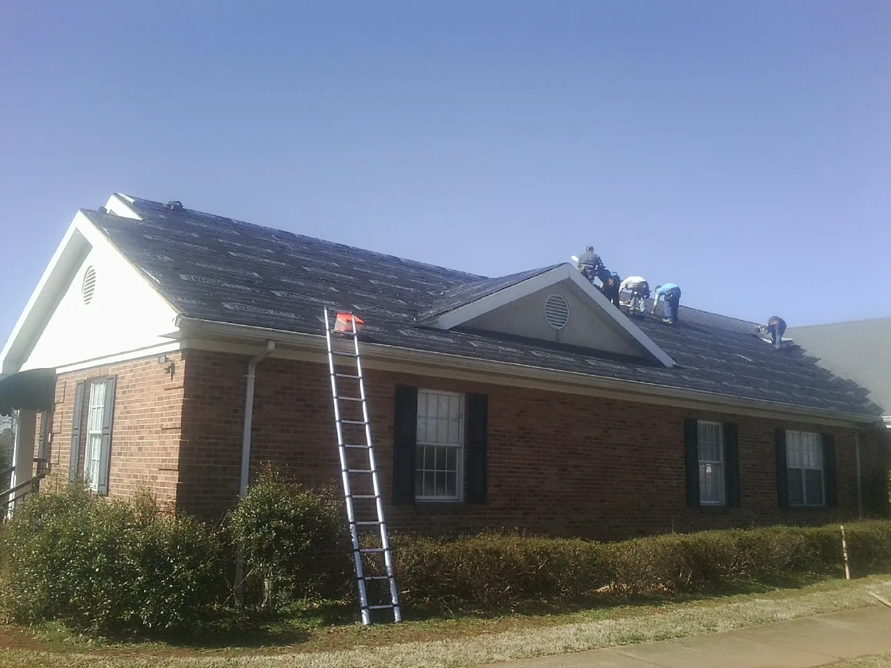 Crew tearing shingles off a brick ranch roof with a ladder set — Emergency Roof Repair work by our crew in Belfast