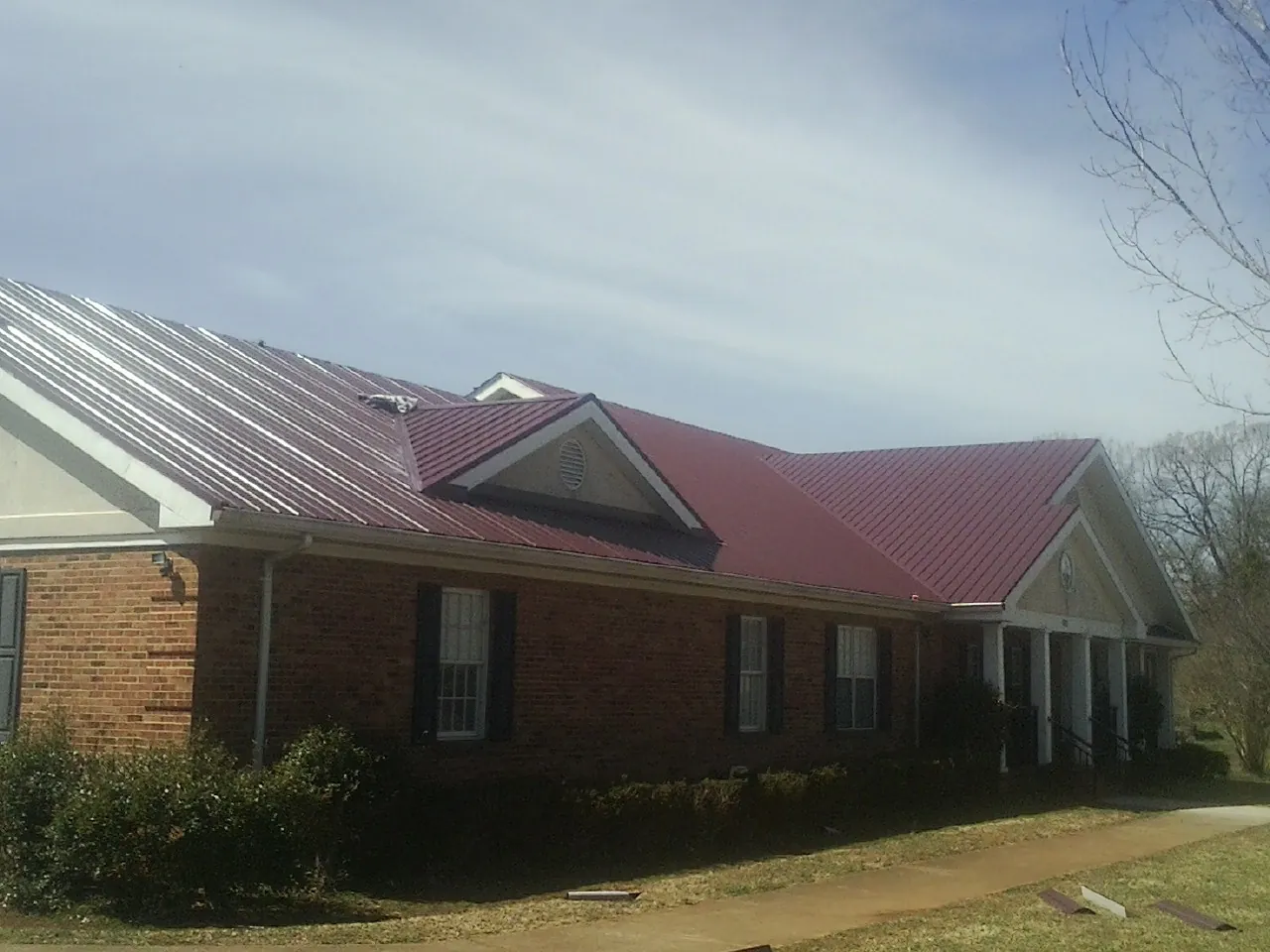 Red metal roof with gabled entries on a long brick building, from a Hail Damage Roof Repair job in Belfast