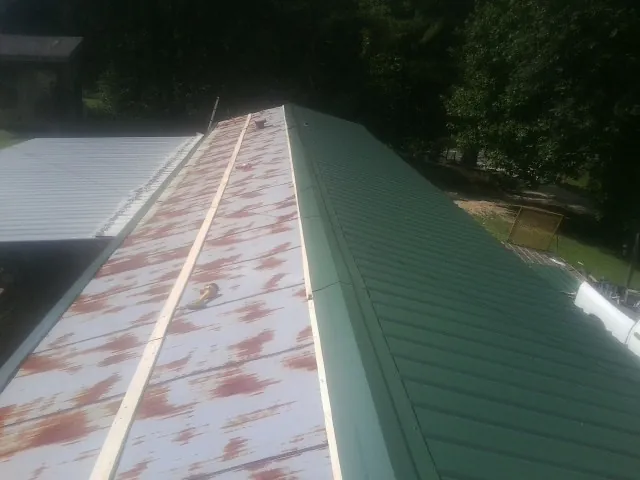 Old rusted panels beside newly installed green metal roofing — Wind Damage Roof Repair by Roofing Brothers in Belfast
