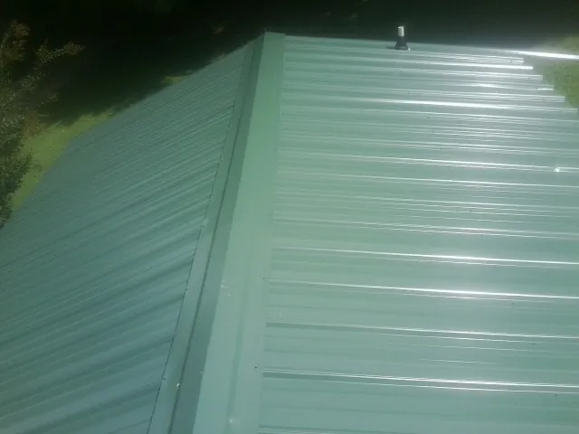 New green metal panels meeting at the ridge of a roof — Flat Roof Repair work by our crew in Belfast